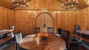 Een kamer met houten lambrisering, een grote ronde tafel, stoelen en een kroonluchter.