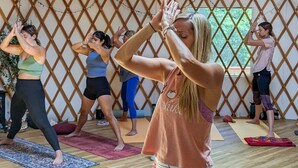 Een groep mensen beoefent yoga in een tent met een houten plafond en lattenwanden.