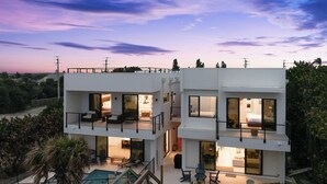 A modern two-story house with a pool, outdoor seating, and a view of the surrounding landscape. - Beachfront Luxe Stay | Pool Access & Rooftop Deck with Stunning Views (Melbourne Beach)