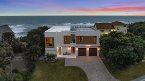A modern two-story house with a garage, situated near a coastline with a view of the ocean. - Beachfront Luxe Stay | Pool Access & Rooftop Deck with Stunning Views (Melbourne Beach)
