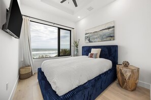Un dormitorio con un ventanal grande, una cama, un cuadro y una mesita de noche de madera.