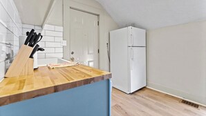 Een keuken met een houten aanrecht, een witte koelkast en een deur op de achtergrond.