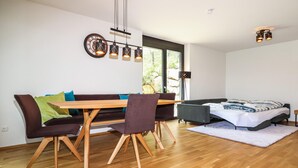 A modern living space with a wooden dining table, cushioned chairs, a sofa, and a bed. - Ferienwohnung mit Terrasse (Bürserberg)