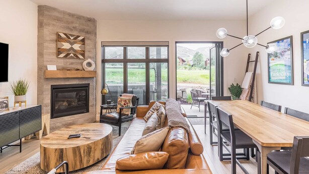 A modern living room with a fireplace, a large window, and a dining area. - Slope Sight by Avantstay A+ Location w/ Hot Tub (Park City)