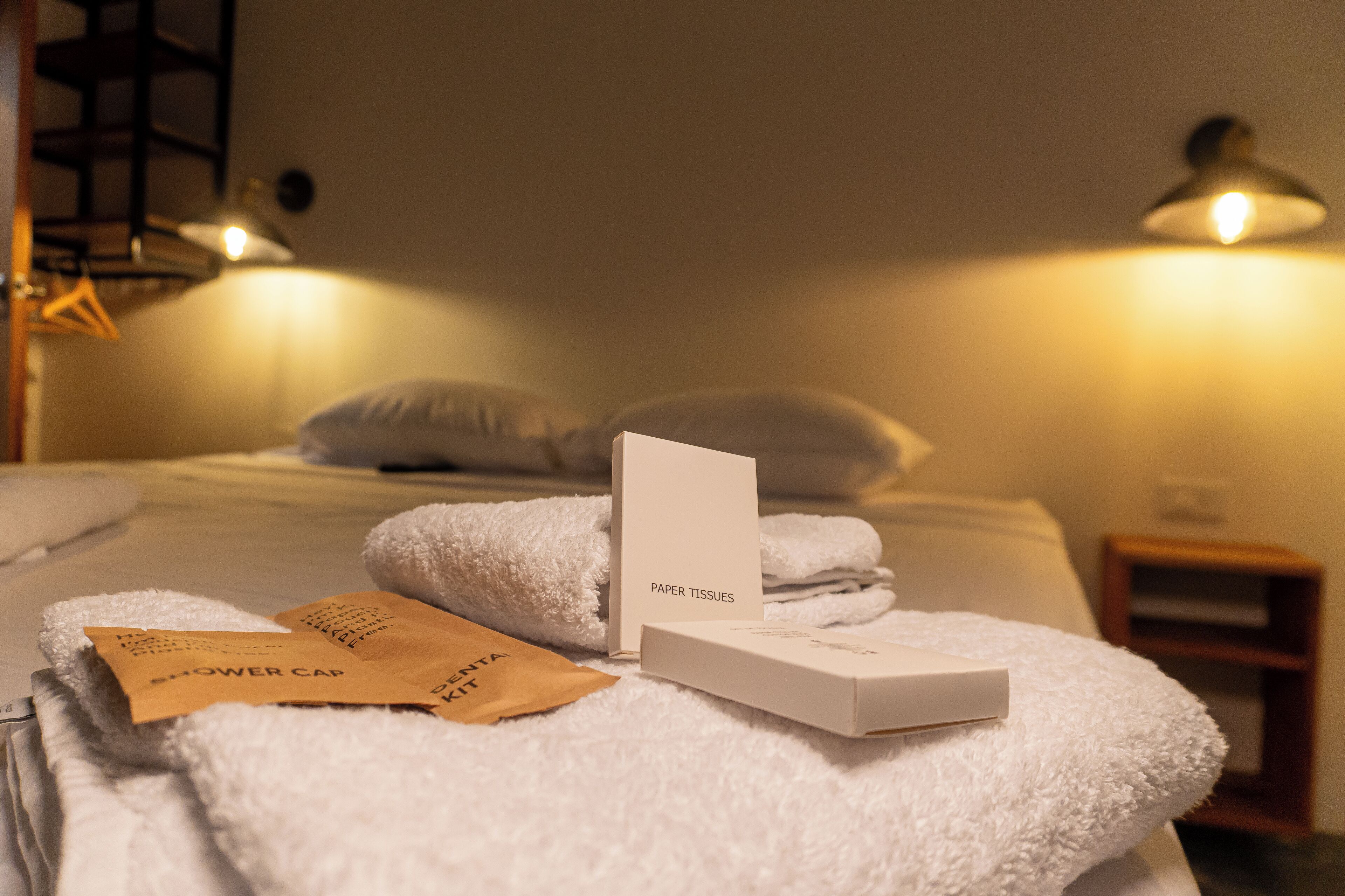 Cama bem arrumada com toalhas brancas, touca de banho e uma caixa de lenços de papel.
