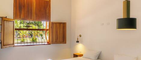 A bedroom with two beds, a window with wooden shutters, a wall-mounted lamp, and a small bedside table.