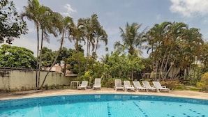 Una piscina con sillas de descanso y palmeras al fondo.