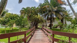 Un puente de madera que lleva a un edificio rodeado de abundante vegetación y palmeras.