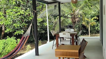 A covered outdoor seating area with a table and chairs, a hammock, and a ceiling fan.
