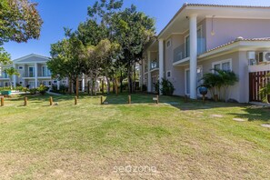 A residential building with a well-maintained lawn, trees, and a clear sky. - Houses in Condominium Near Pitinga Beach - MGI (Porto Seguro)