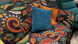 A colorful patterned sofa with a blue pillow, a teal armchair, and a white couch in a modern living room with a potted plant and wall decorations. - Miller House Carriage House Studio (mahone bay)