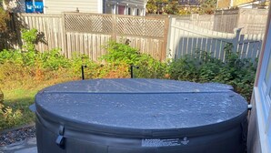 A hot tub in a backyard with a stone patio, a small table, and a blanket. - Miller House Carriage House Studio (mahone bay)