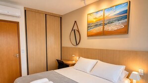 Ett hotellrum med en säng, ett skrivbord, en stol, en tavla som hänger på väggen och en sänglampa.