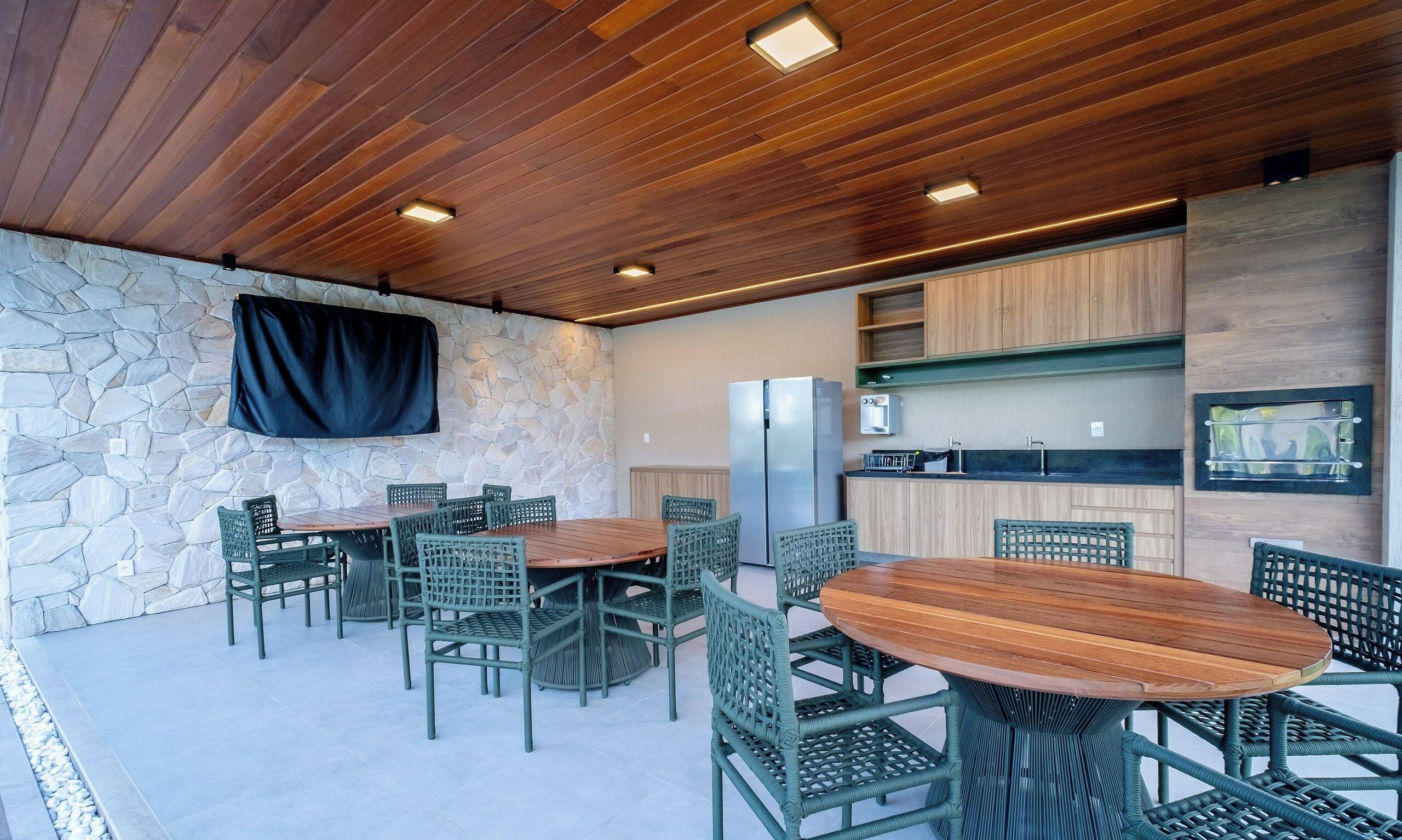 A modern outdoor kitchen area with a stone wall, wooden ceiling, and a dining set.