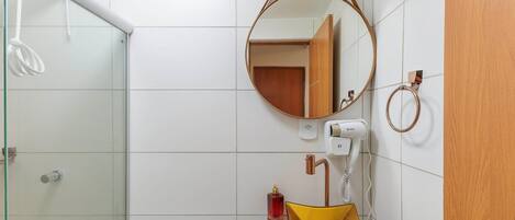 A bathroom with a glass shower enclosure, a wooden door, a round mirror, and a yellow sink with a glass basin.