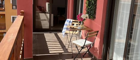 A balcony with a table, chairs, and a potted plant.