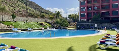 Una piscina con sillones de descanso, un muro de piedra y un edificio con balcones.
