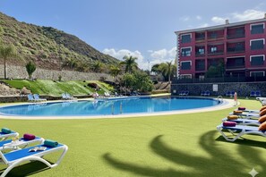 A swimming pool with lounge chairs, a stone wall, and a building with balconies.