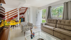 Un salon moderne avec un canapé, une table basse en verre et un coin repas avec des chaises jaunes.