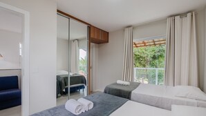 Une chambre d’hôtel avec deux lits, un canapé, une porte coulissante et une vue sur la verdure.