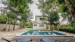 Une maison moderne avec une piscine, entourée d’arbres et d’un mur de pierre.