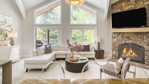 A modern living room with a stone fireplace, large windows, and a comfortable seating area. - Deer Valley Delight by Avantstay Deer Valley Retreat + Spa (Park City)