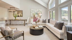 A spacious living room with a white sofa, a round coffee table, and a dining area with clear chairs and a glass table. - Deer Valley Delight by Avantstay Deer Valley Retreat + Spa (Park City)
