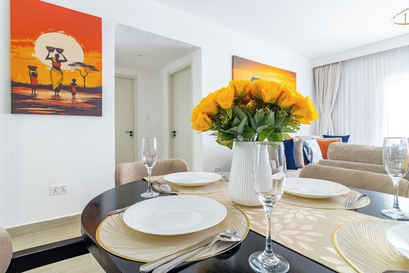 A dining area with a table set for four, a vase of yellow flowers, and two paintings on the wall.