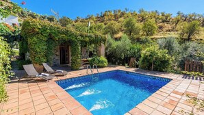 A rectangular swimming pool with a tiled edge, surrounded by a brick patio. There are two lounge chairs and a small wooden structure with a door. - La Terrera Órgiva by Ruralidays (Granada)
