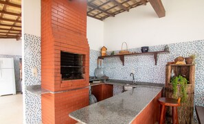 A kitchen with a brick oven, tiled backsplash, and wooden shelves.