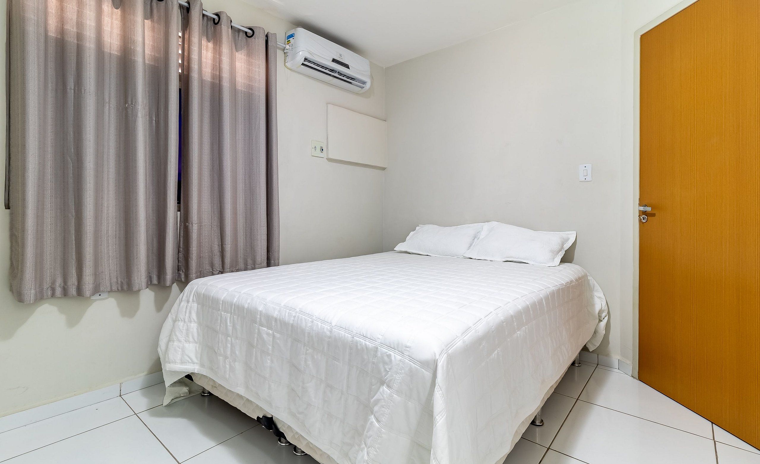 Un dormitorio con cama, cortinas, un equipo de aire acondicionado y una puerta de madera.
