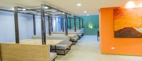 A modern interior with long tables and benches, a bright orange wall, and a sunset painting.