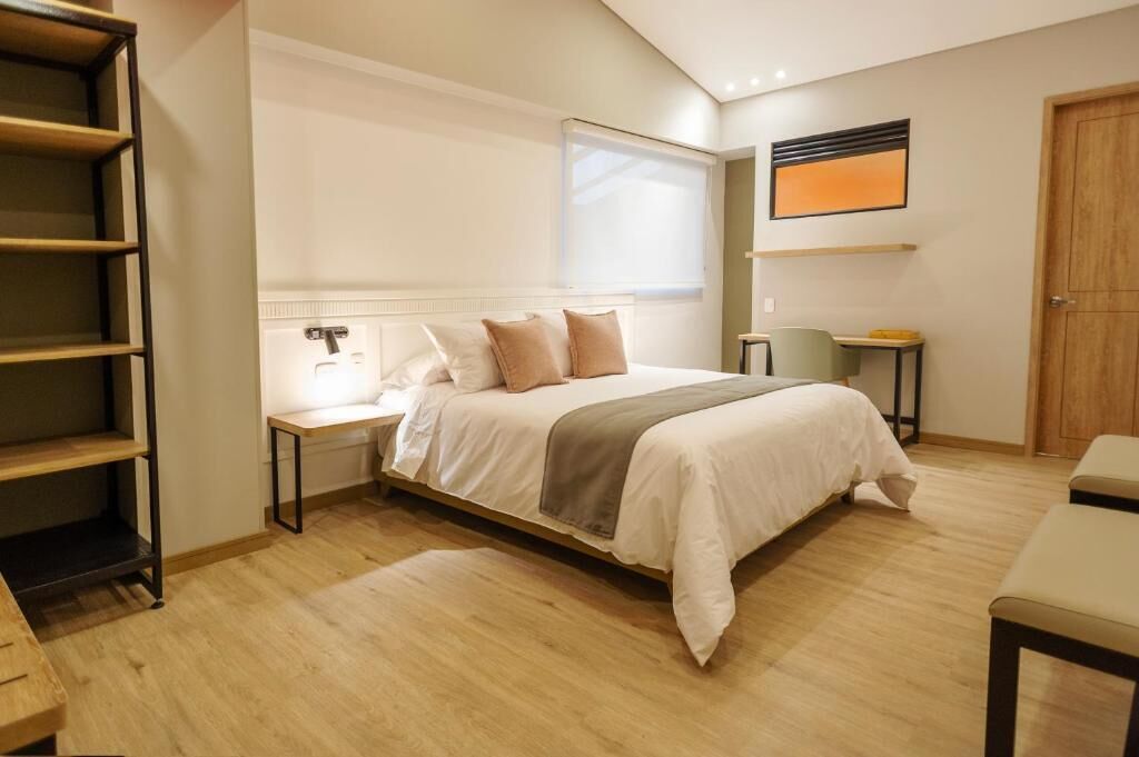 A bedroom with a bed, bedside tables, a desk, a chair, a wardrobe, and a window.