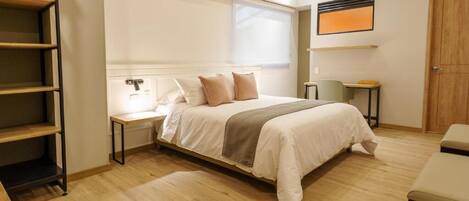 A bedroom with a bed, bedside tables, a desk, a chair, a wardrobe, and a window.