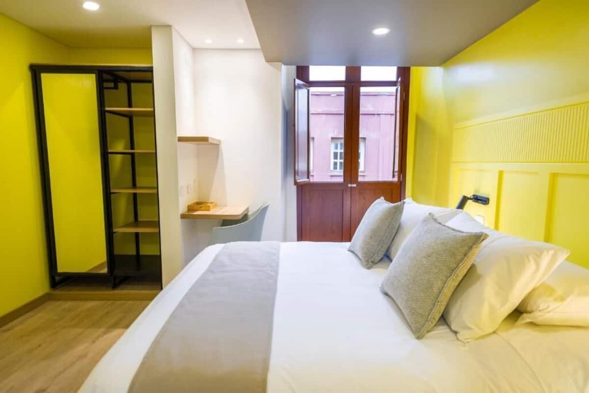 A hotel room with a bed, a desk, and a window with a view of a building.