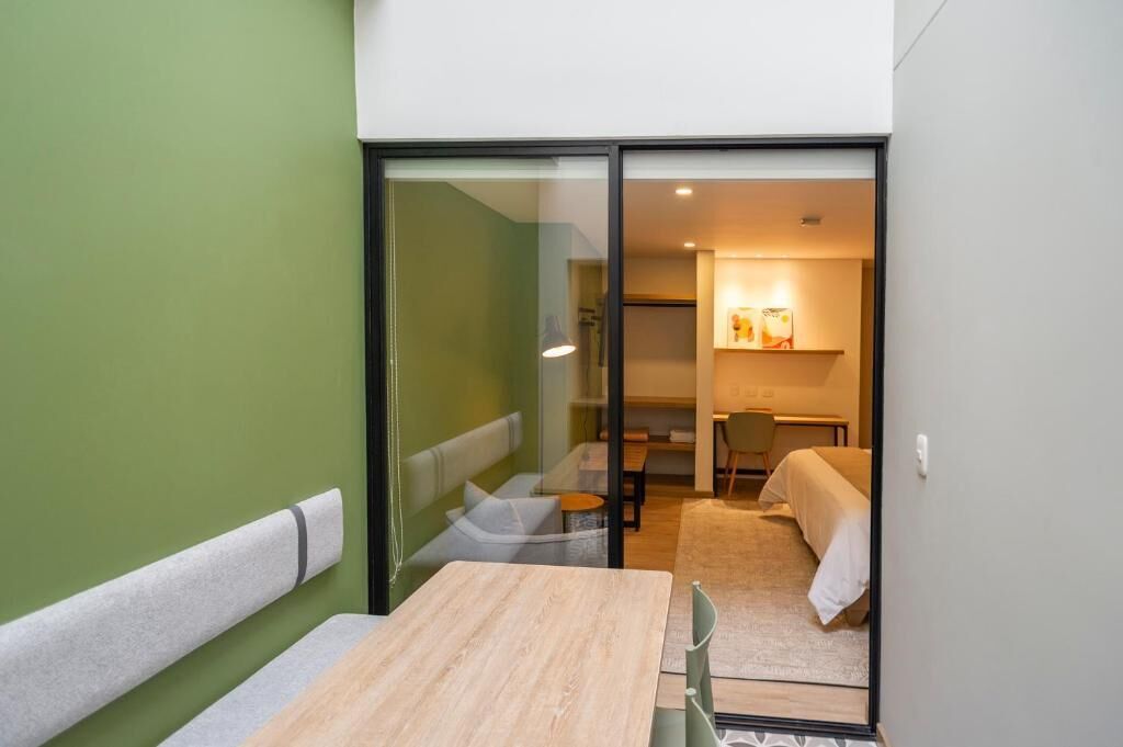 Una habitación compacta con una mesa de madera y banco, una cama y una pequeña zona de kitchenette.