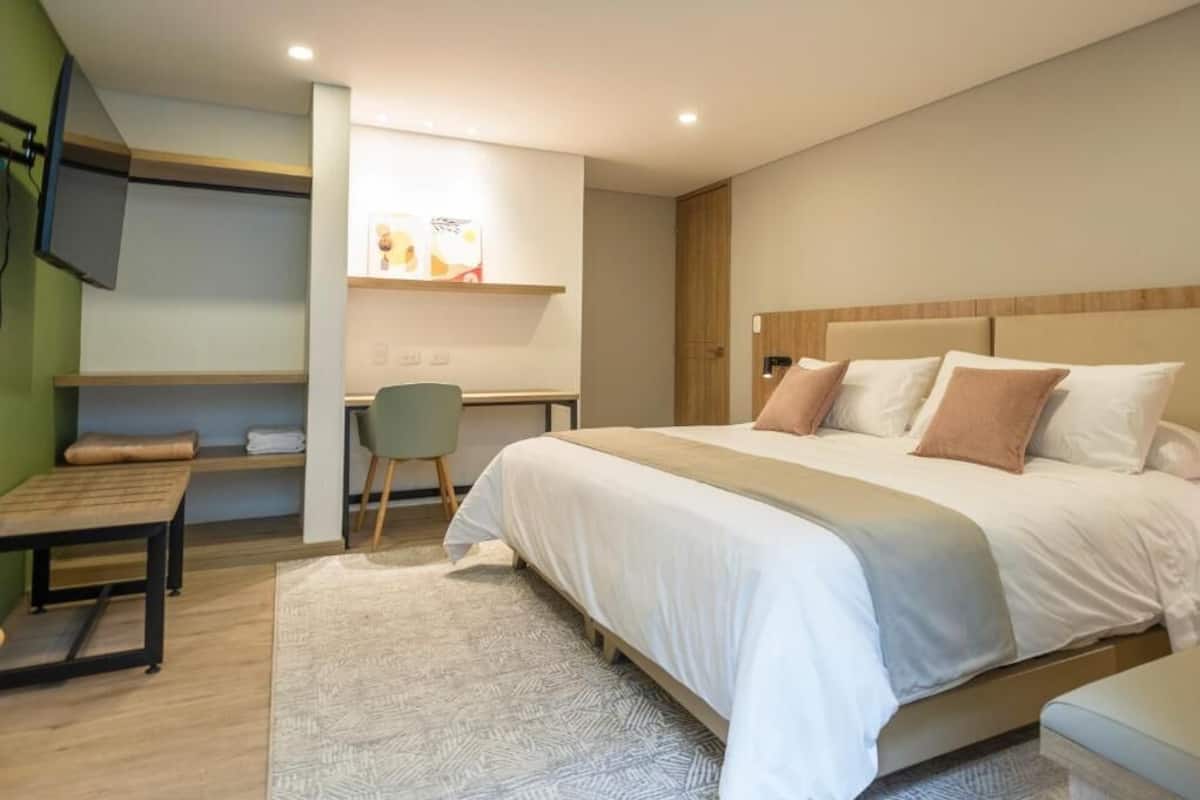 A modern hotel room with a large bed, a desk, and a television mounted on the wall.