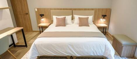 Un dormitorio ordenado con una cama grande, dos mesitas de noche con lámparas, un banco y una mesita auxiliar.