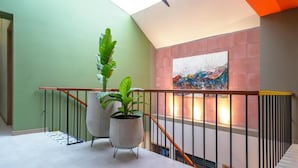 Una escalera moderna con techo de vidrio, una planta en maceta y un cuadro abstracto de colores en la pared.