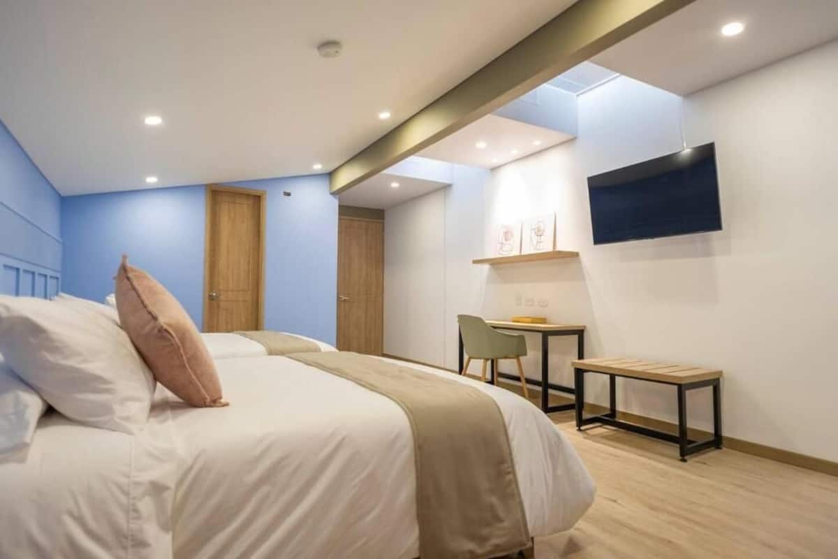 A modern hotel room with a bed, a desk, and a TV mounted on the wall.