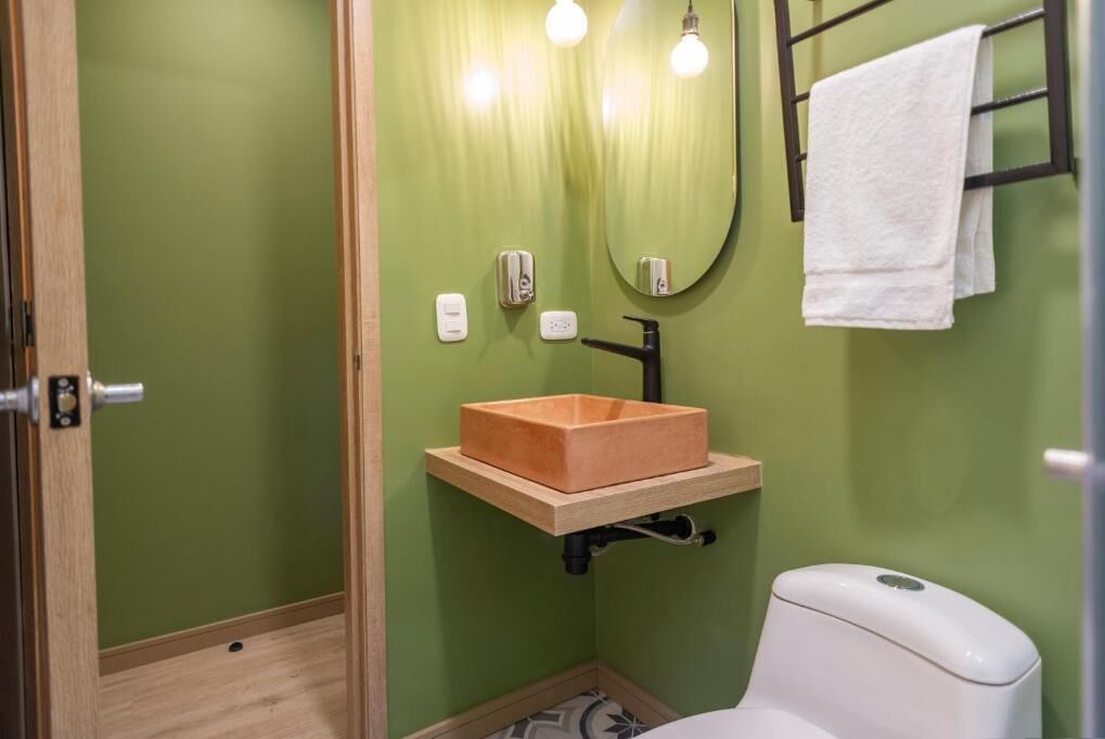 A bathroom with a green wall, a wooden sink, a white toilet, and a towel rack.