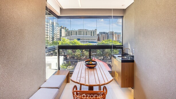 A balcony with a wooden table and chairs, a bowl of fruit, and a view of buildings and trees. - Apt With Pool 200m From the Beach Skc0414 (Maceió)