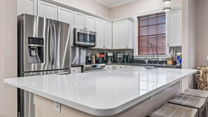 A modern kitchen with stainless steel appliances, a large island, and a window with blinds. - Inviting 5BR Villa in Reunion Resort (Kissimmee)