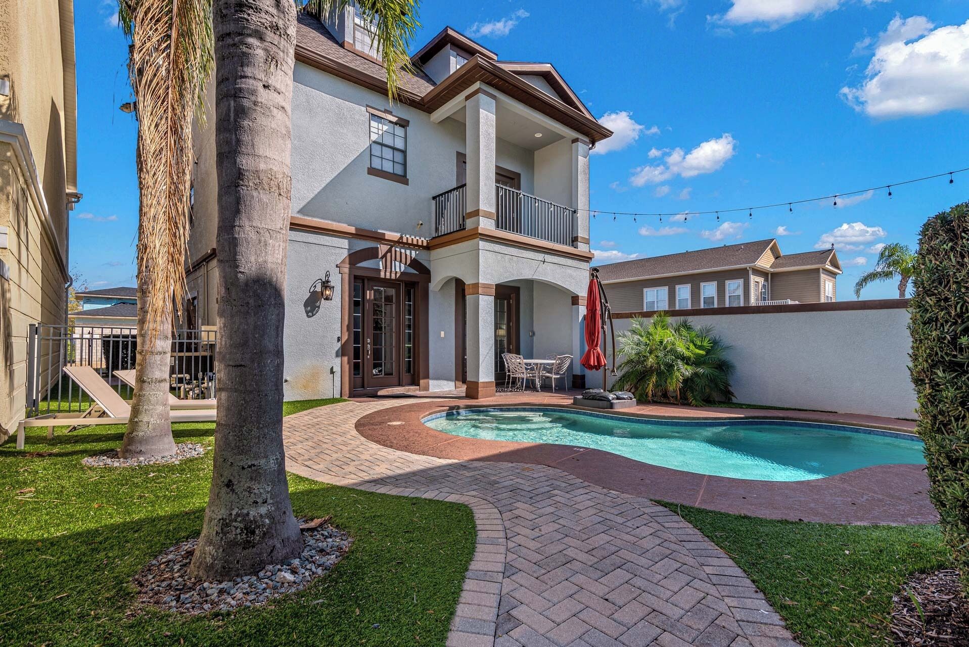 A two-story house with a swimming pool, a covered patio, and a fenced backyard.