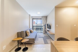 Ein modernes Wohnzimmer mit einer Couch, zwei kleinen Tischen, einem Fernseher und einem Balkon mit Blick.