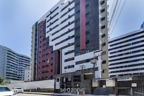 Ein mehrgeschossiges Gebäude mit moderner Architektur, das eine Kombination aus weißen und dunklen Fassadenplatten sowie ein markantes vertikales Element in der Mitte zeigt.
