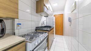 Een keuken met witte betegelde wanden, een gasfornuis, een magnetron en een houten kast.