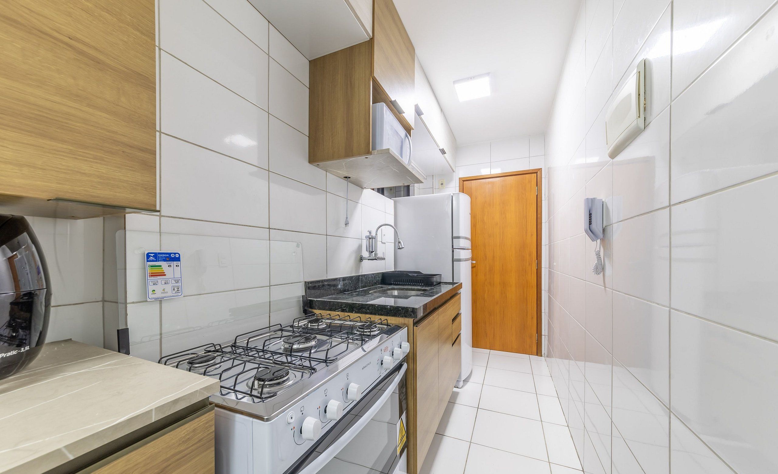 Una cocina con paredes de azulejos blancos, una estufa a gas, un microondas y un armario de madera.