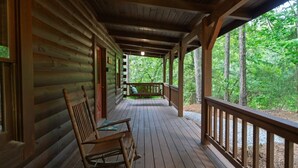 A wooden cabin with a covered porch and a view of a forest.