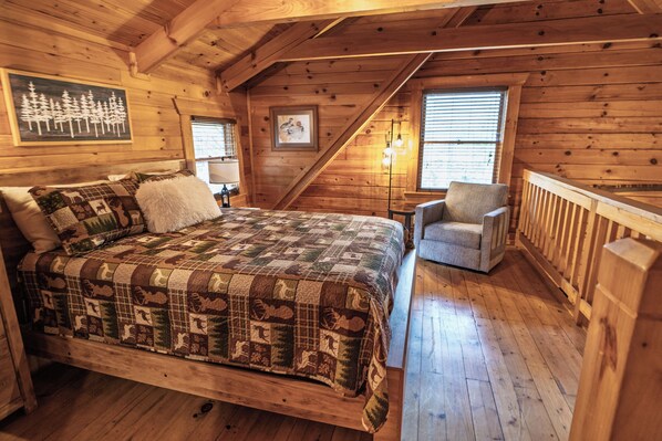 Un dormitorio de cabaña de madera con una cama grande, una silla y una ventana con persianas.